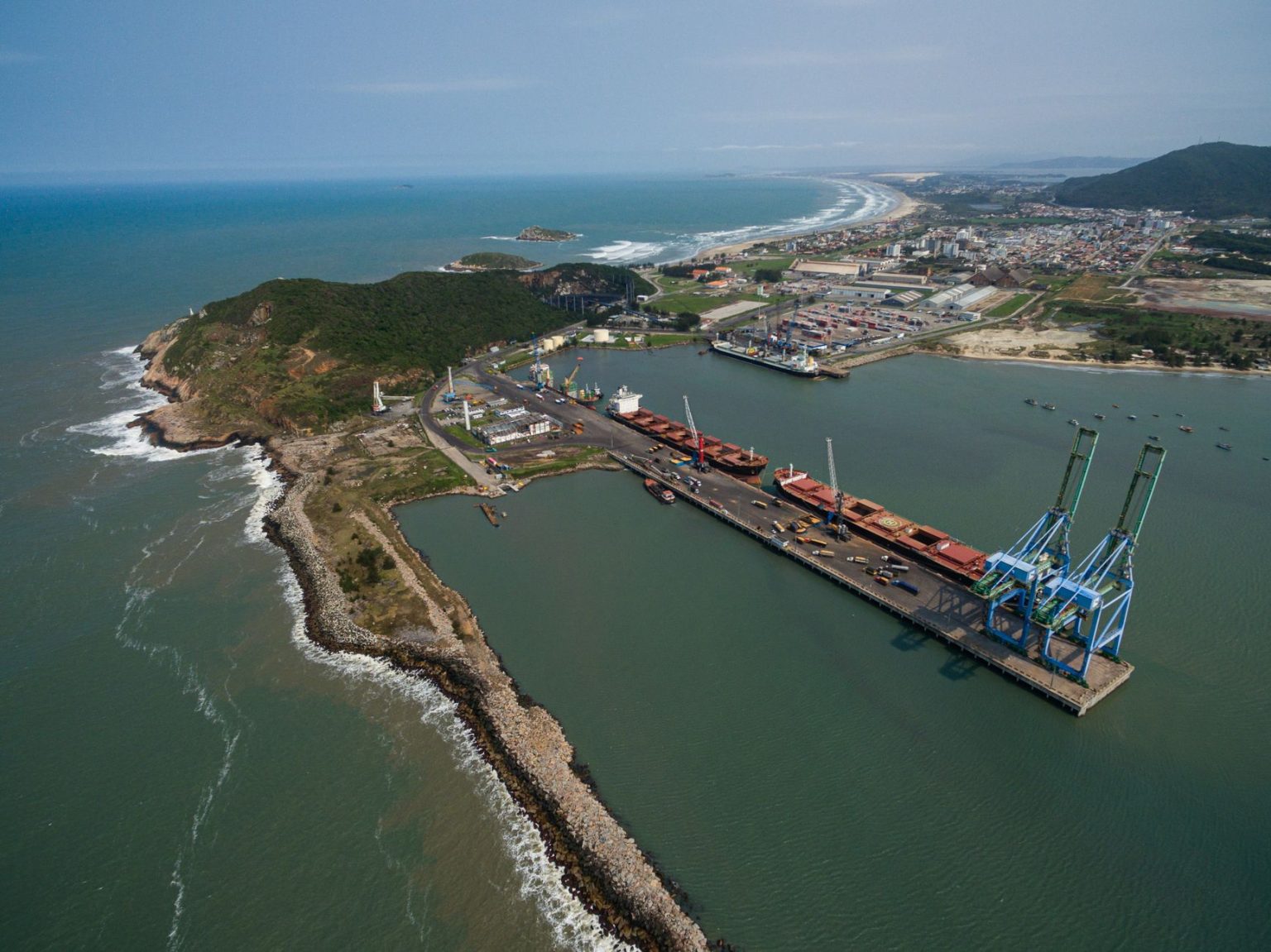 Vista aérea do Porto de Imbituba, com docas, guindastes e a faixa costeira.