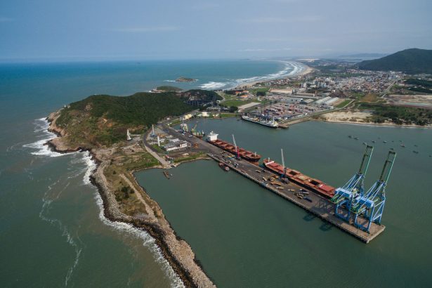 Vista aérea do Porto de Imbituba, com docas, guindastes e a faixa costeira.