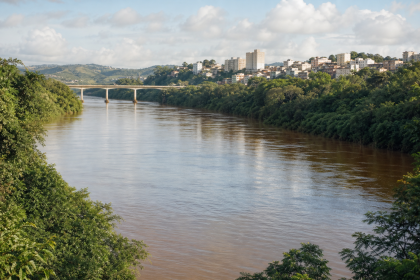 Rio Doce em área de município mineiro, com vegetação às margens e estrutura urbana ao fundo