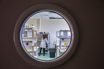 Cientista trabalha em um laboratório moderno, observado através de uma janela circular.