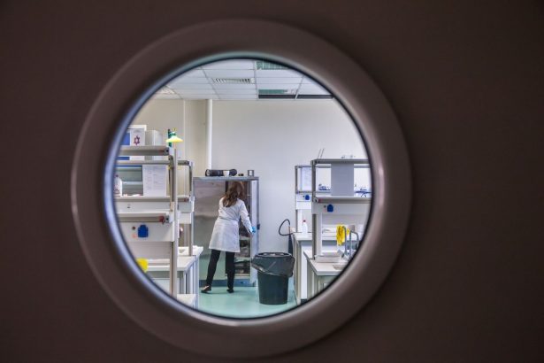 Cientista trabalha em um laboratório moderno, observado através de uma janela circular.