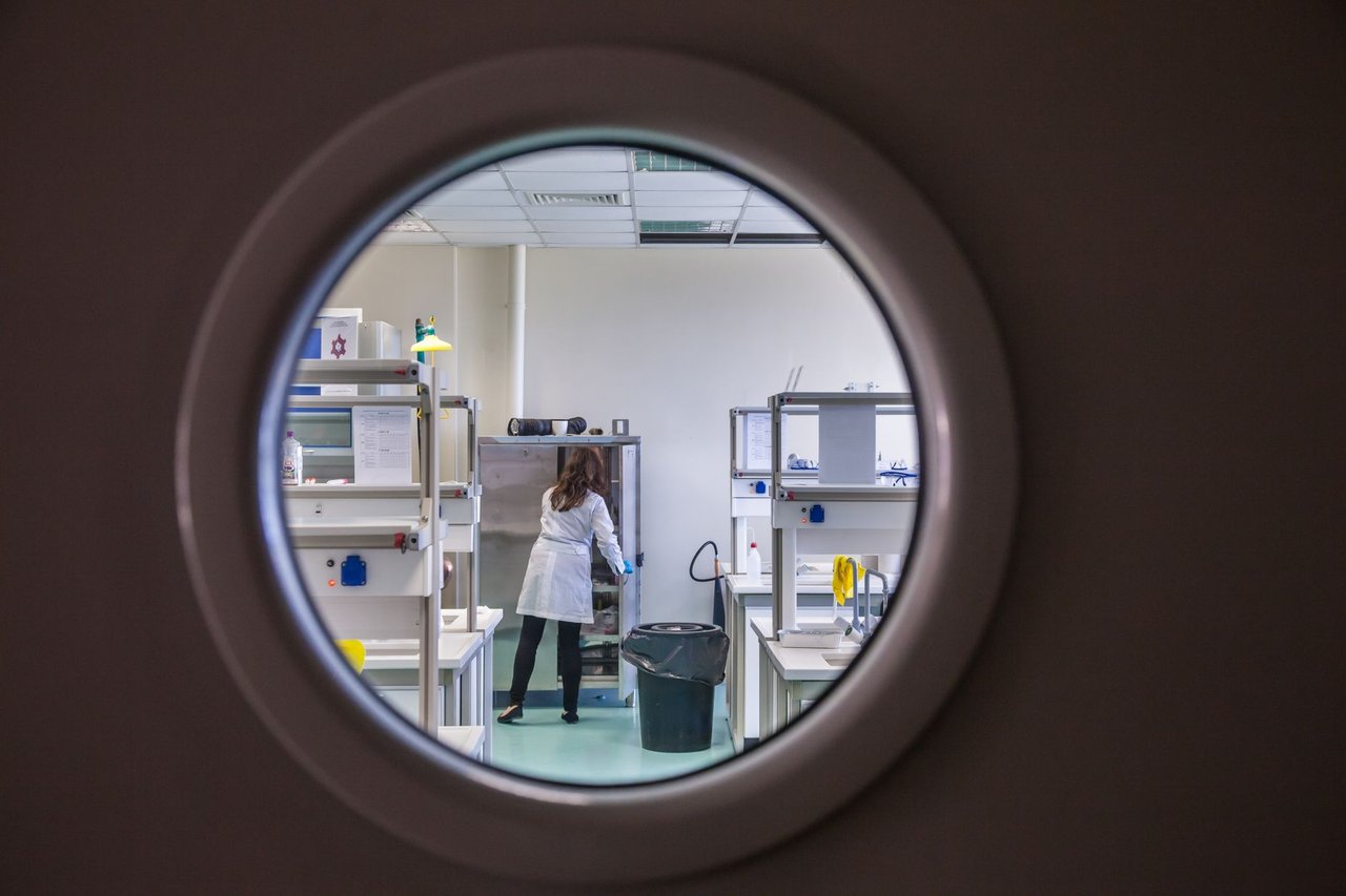 Cientista trabalha em um laboratório moderno, observado através de uma janela circular.