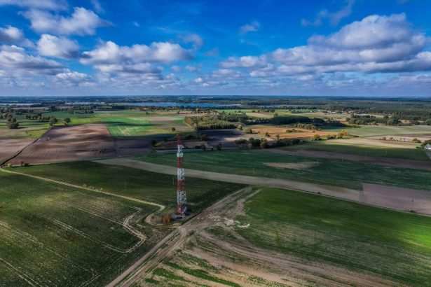 Torre de comunicação isolada em meio a uma extensa área rural, sob céu azul com nuvens.